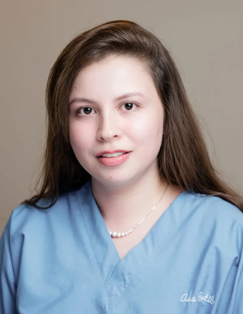 A woman in blue scrubs is smiling for the camera.