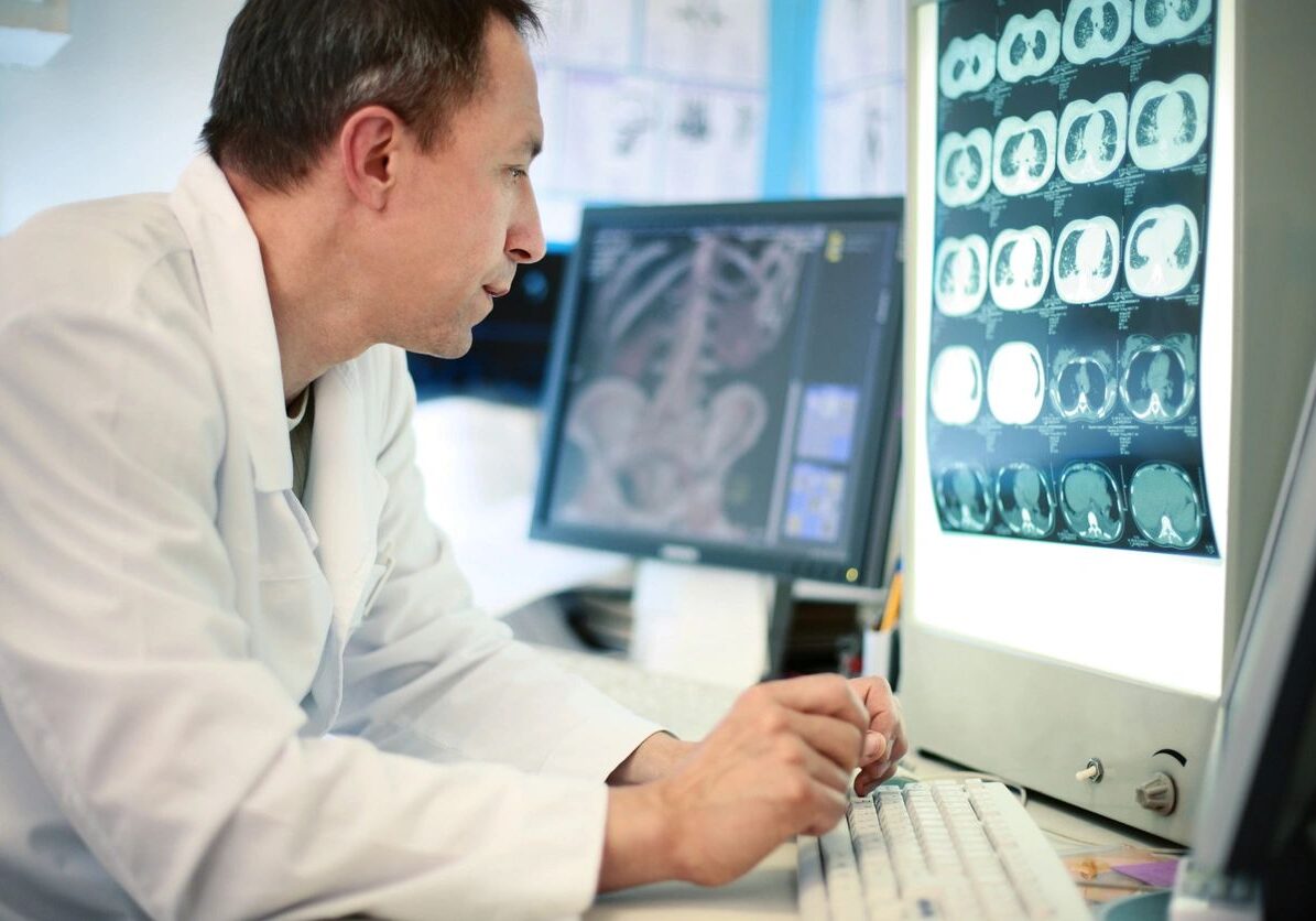 A man in white lab coat looking at computer screen.